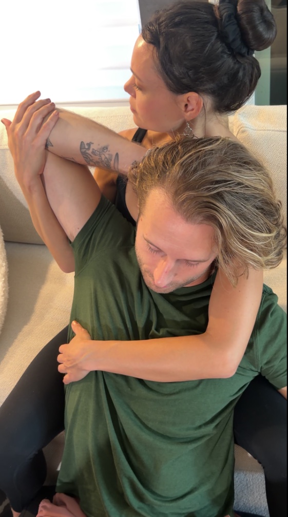 Two women sitting on a couch, one hugging the other, with one woman holding her arm.