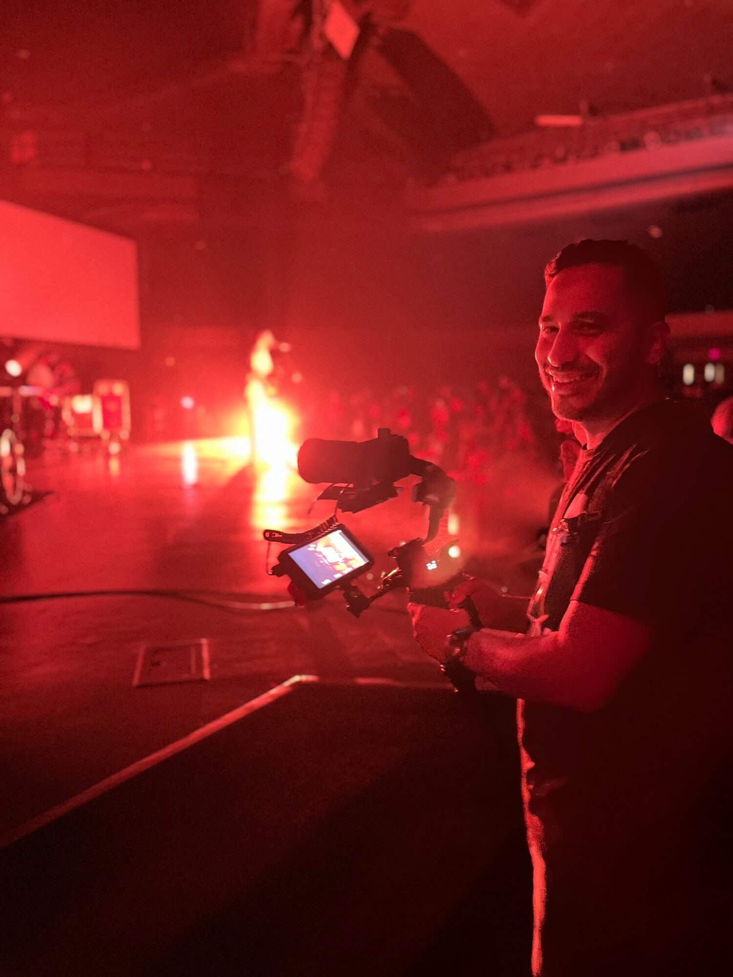 Person holding a camera in a dimly lit venue with red lighting and a bright fire or light source in the background.