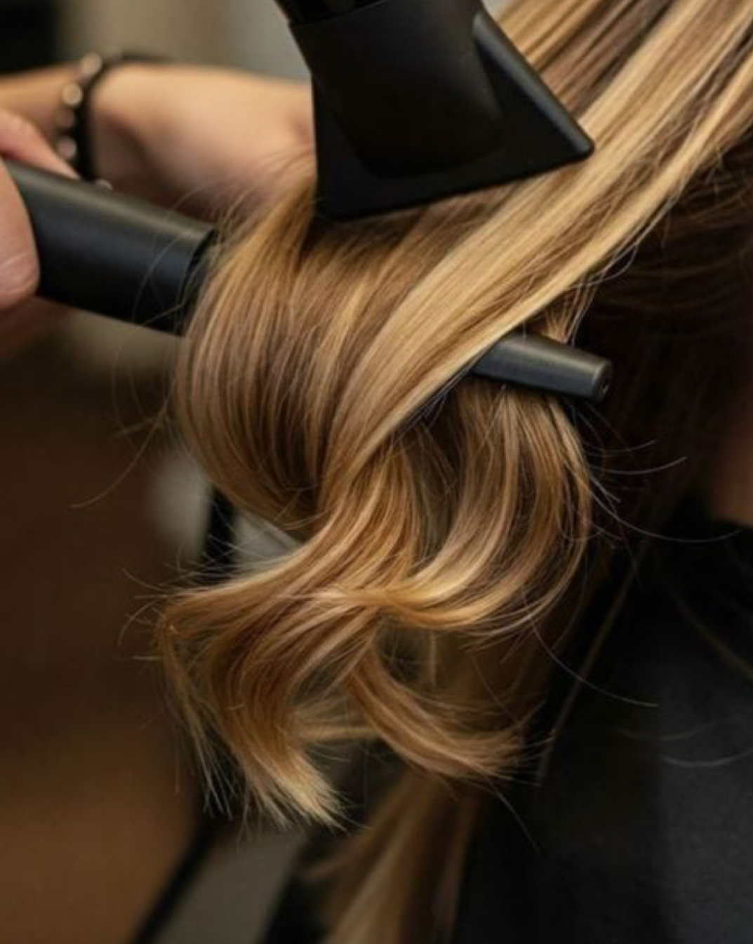 Person's hair being styled with a curling iron, hair is long and blonde, in a salon setting.