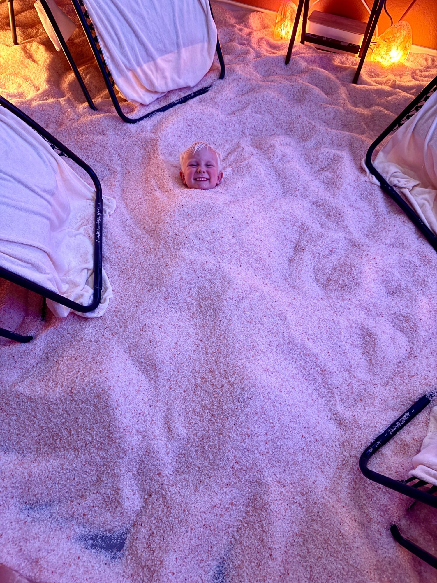 Baby's head peeking out from sand, surrounded by beach chairs and warm lighting.