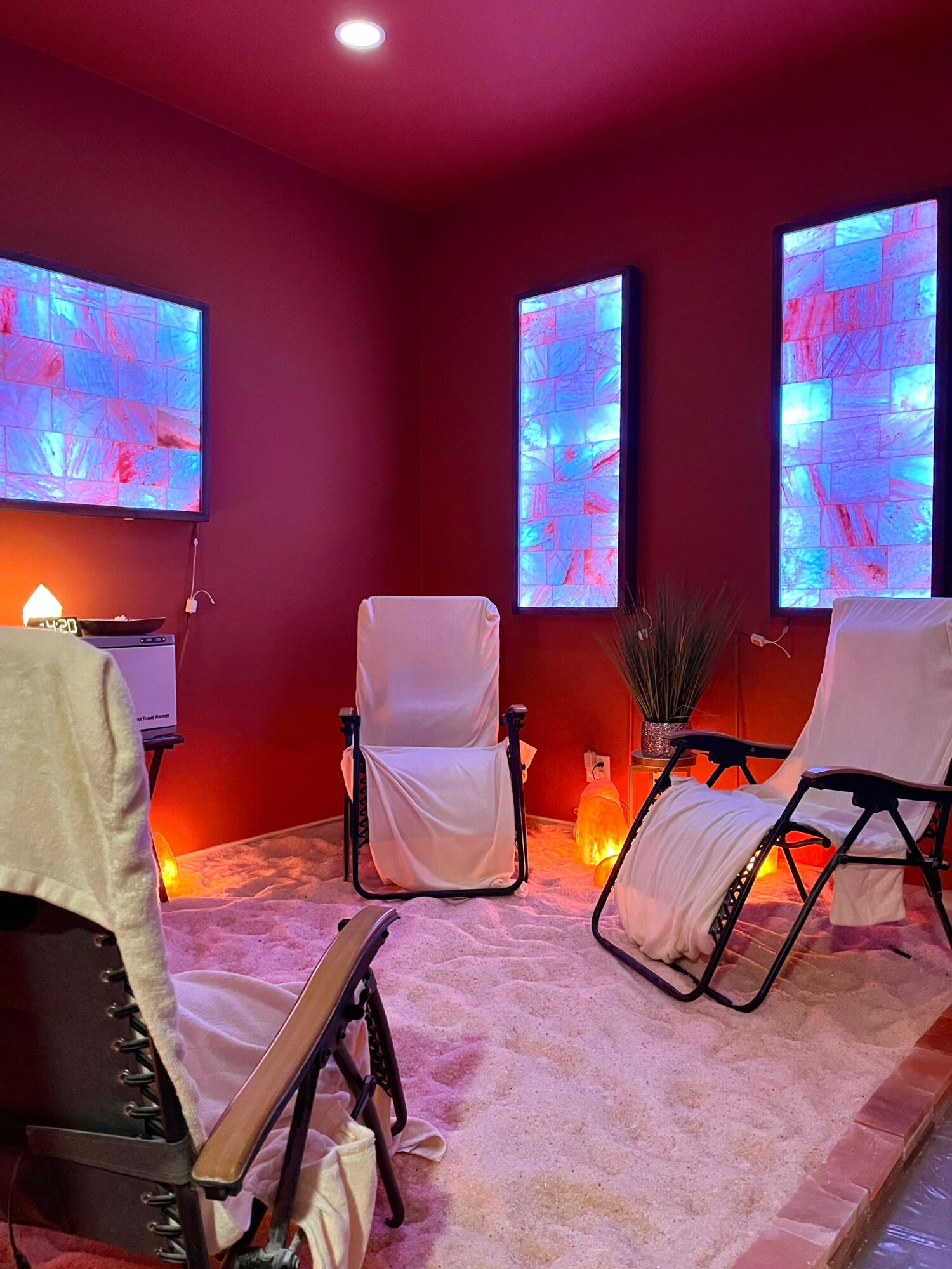 Room with pink walls, three colorful abstract wall art pieces, two white lounge chairs, a plant, and a soft pink rug.