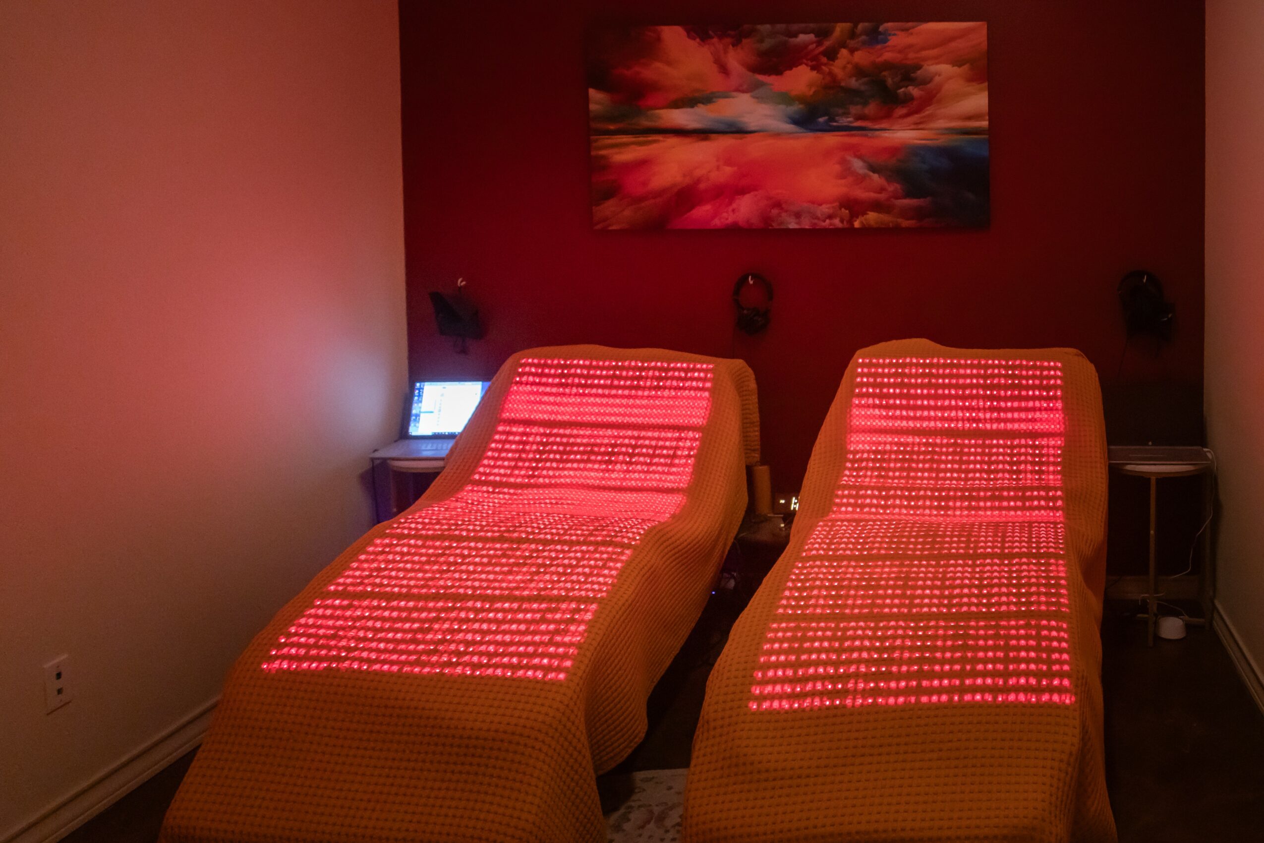 Two lounge chairs with red patterned cushions in a room with red walls and a colorful painting above.