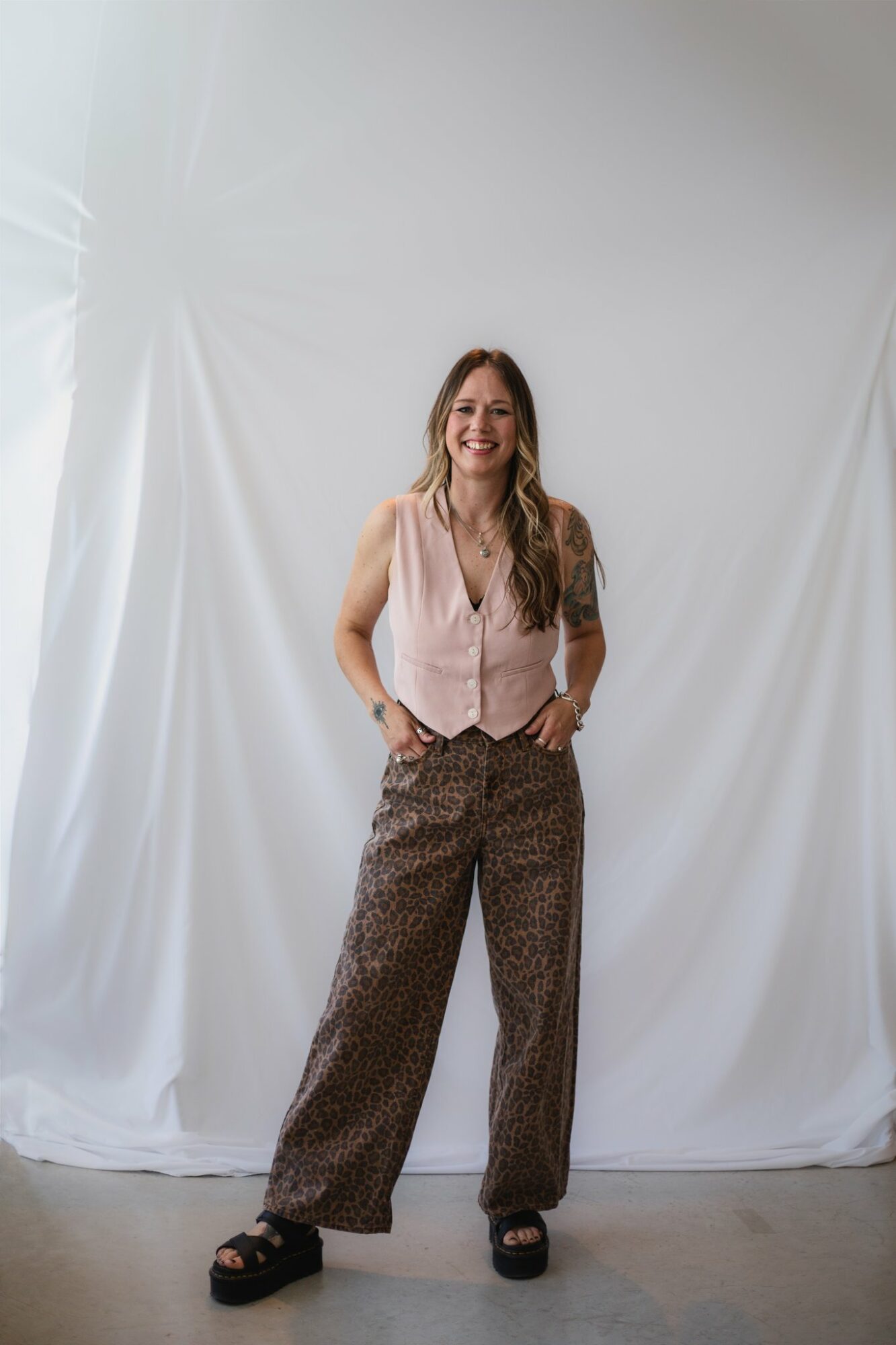 Woman standing with hands in pockets, smiling, in front of a white backdrop.