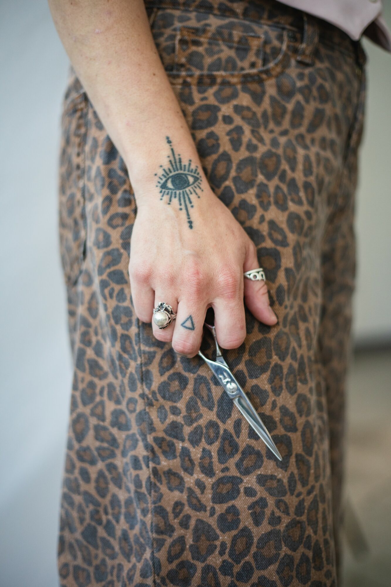 Person's hand with multiple rings, holding a small knife, tattoo on wrist, wearing leopard print pants.
