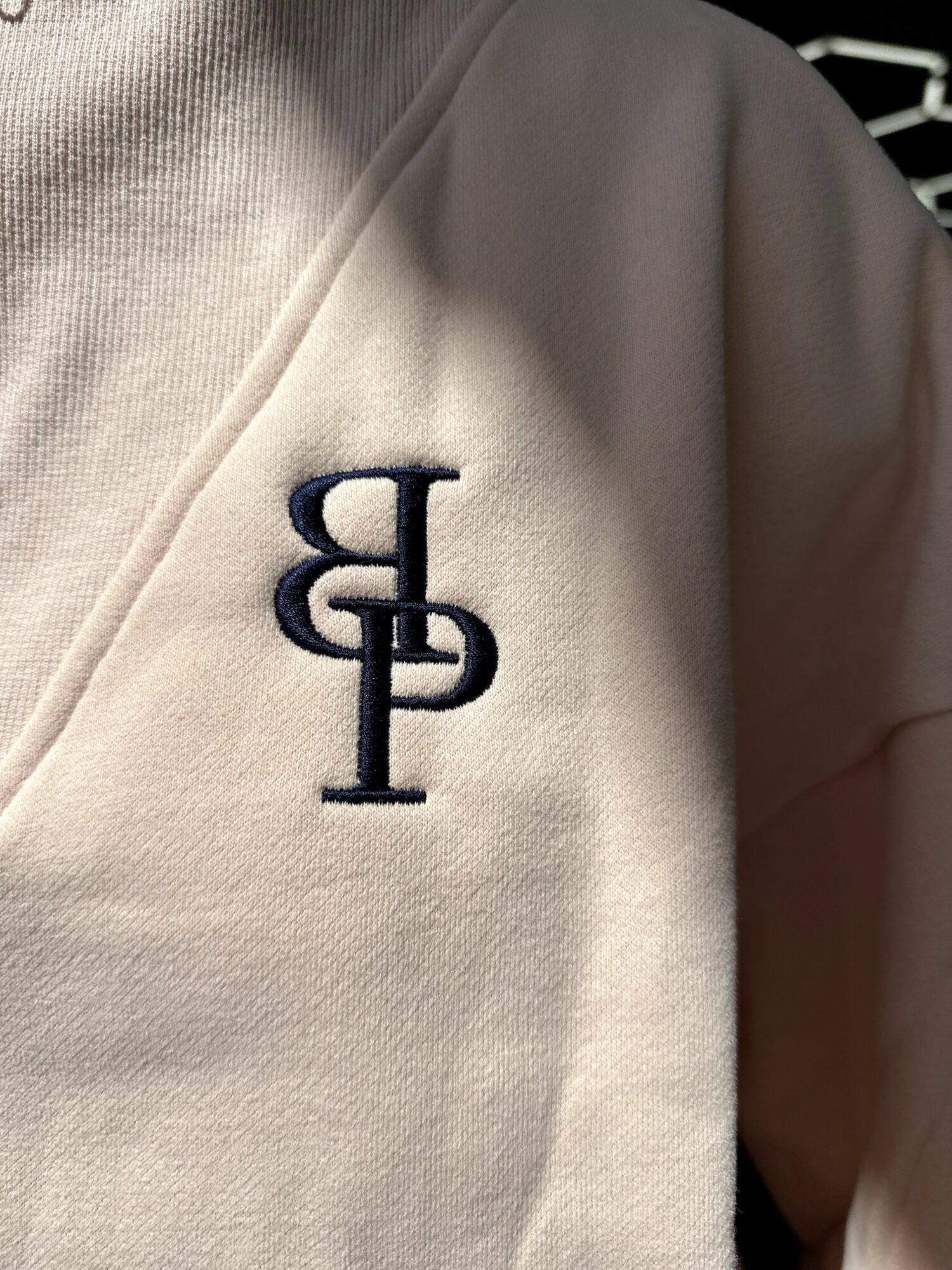 Close-up of a beige garment with a navy embroidered logo of intertwined letters.