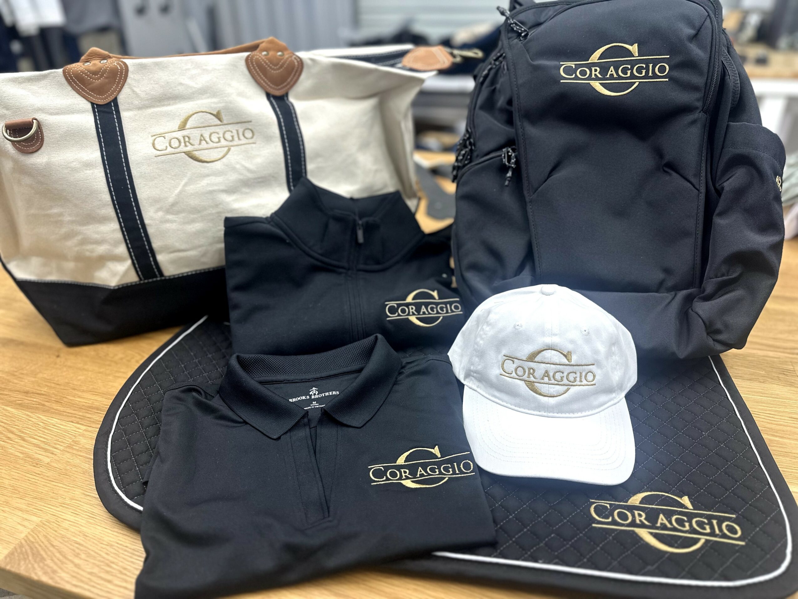 Collection of bags, a cap, and clothing items with 'Cor Aggio' branding on a wooden surface.