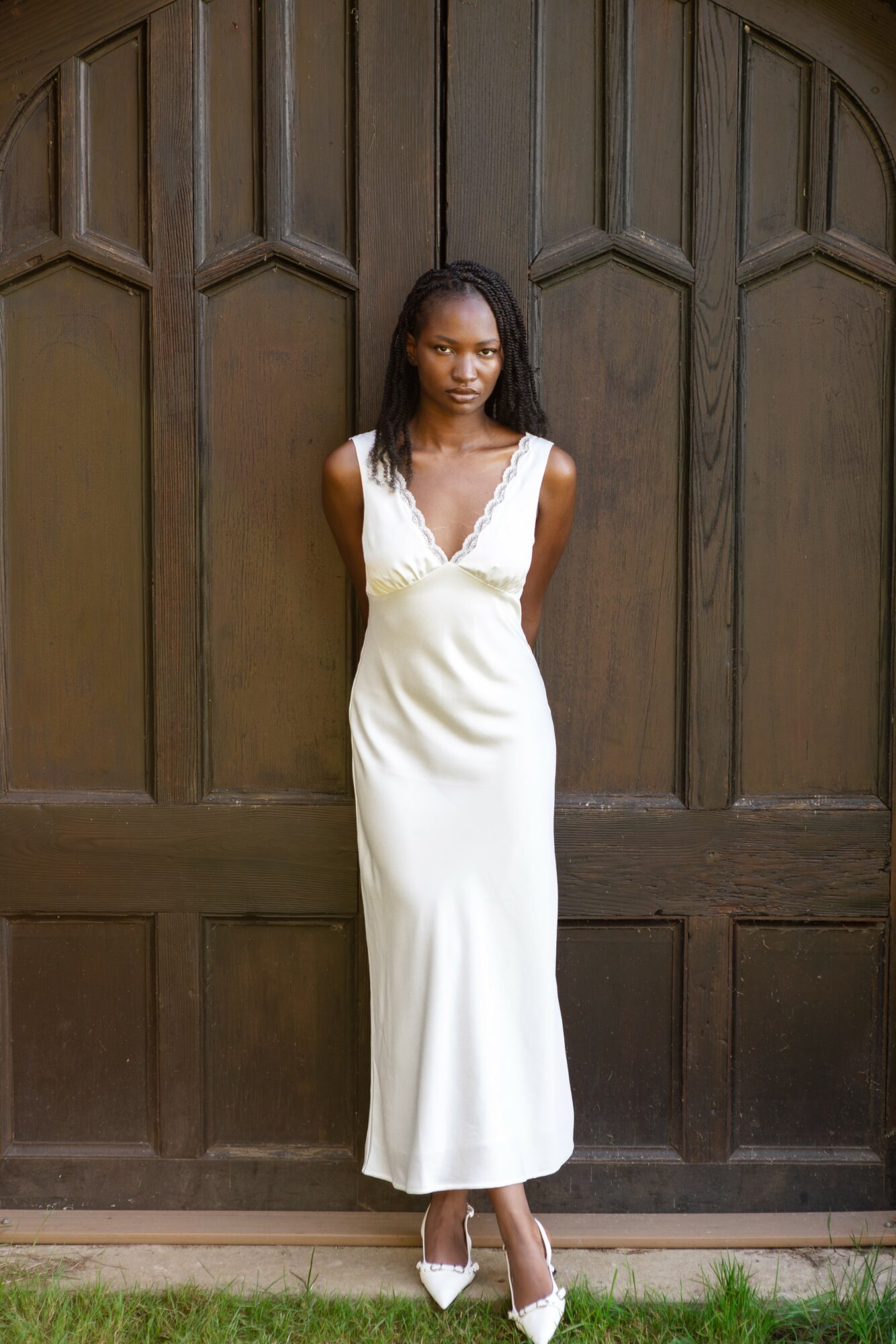 Woman in white dress standing in front of wooden door with geometric panels.