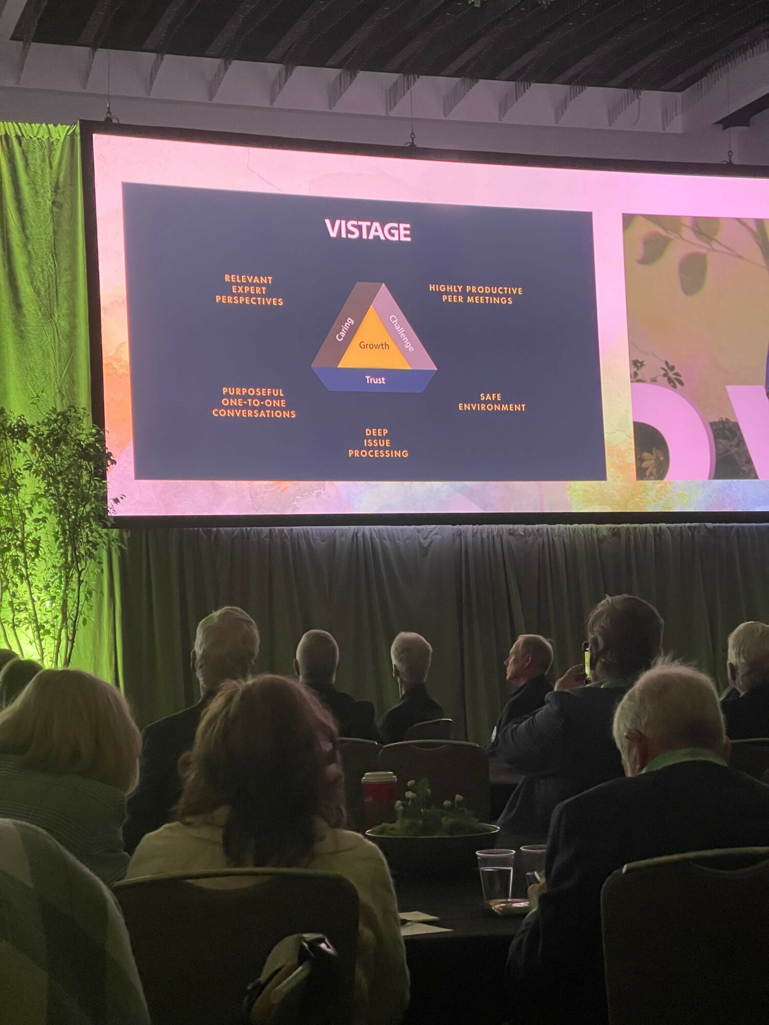 Audience watching a presentation slide with a pyramid diagram on a large screen in a conference room.
