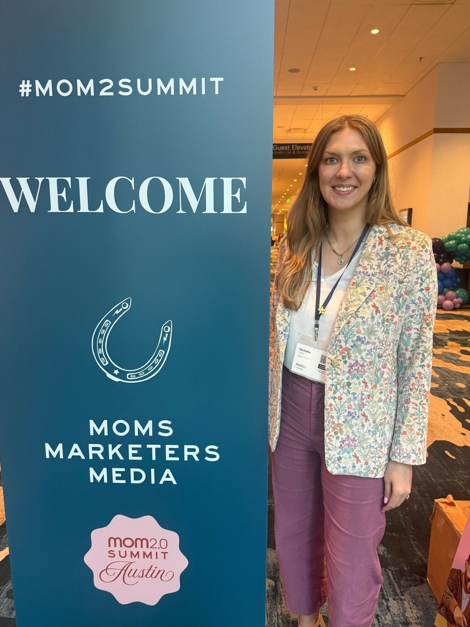 Woman standing next to a blue banner with event information, smiling, in an indoor setting.