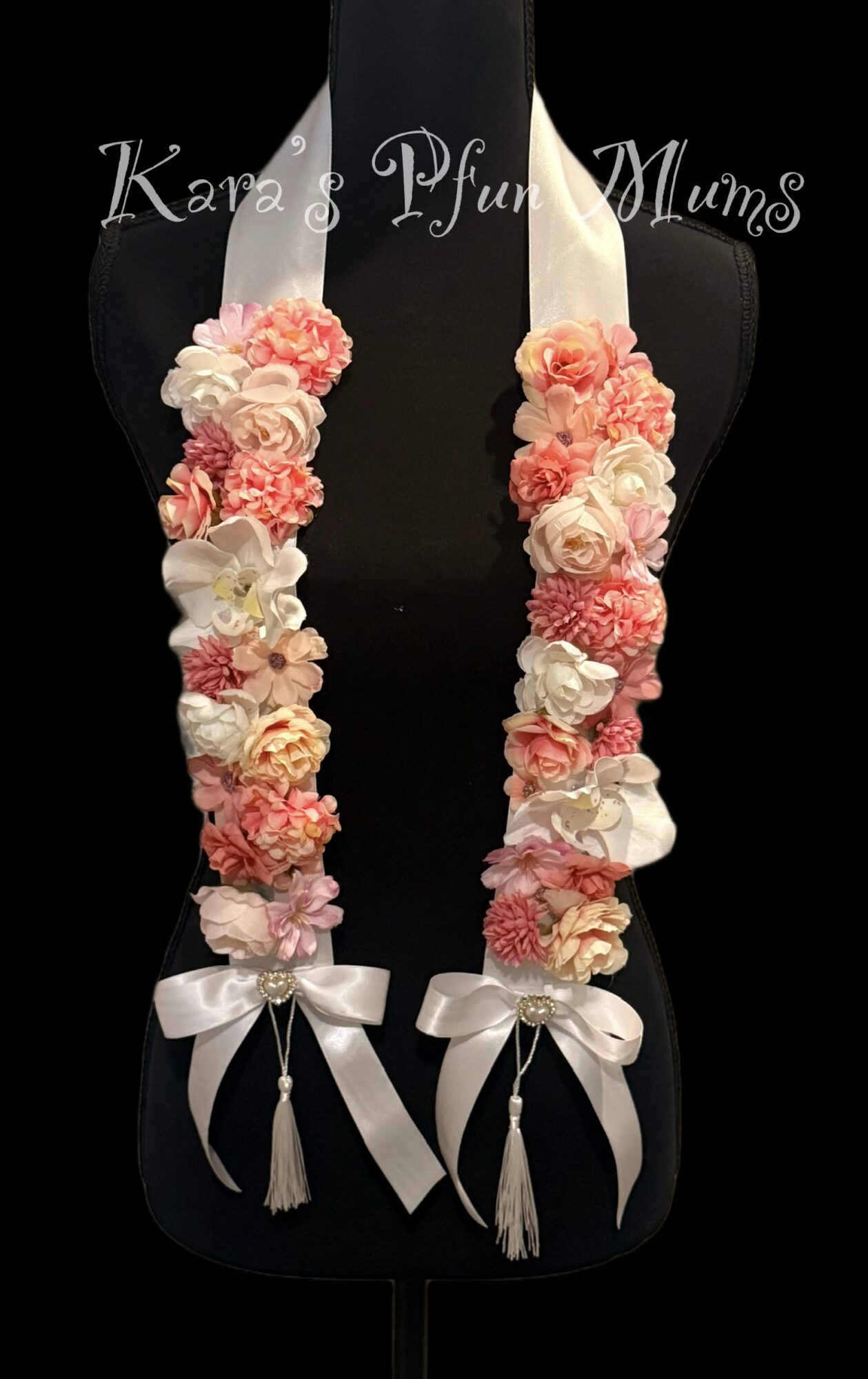 Two floral garlands with pink and white flowers, white ribbons, and tassels hang against a black background.