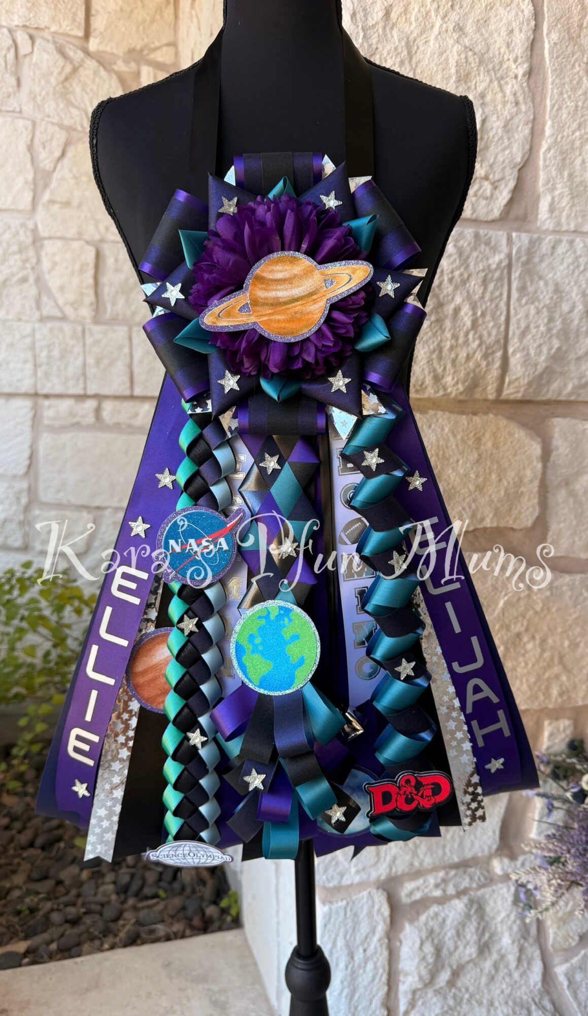 Decorative NASA-themed ribbon and planet ornament on black mannequin bust against stone wall.