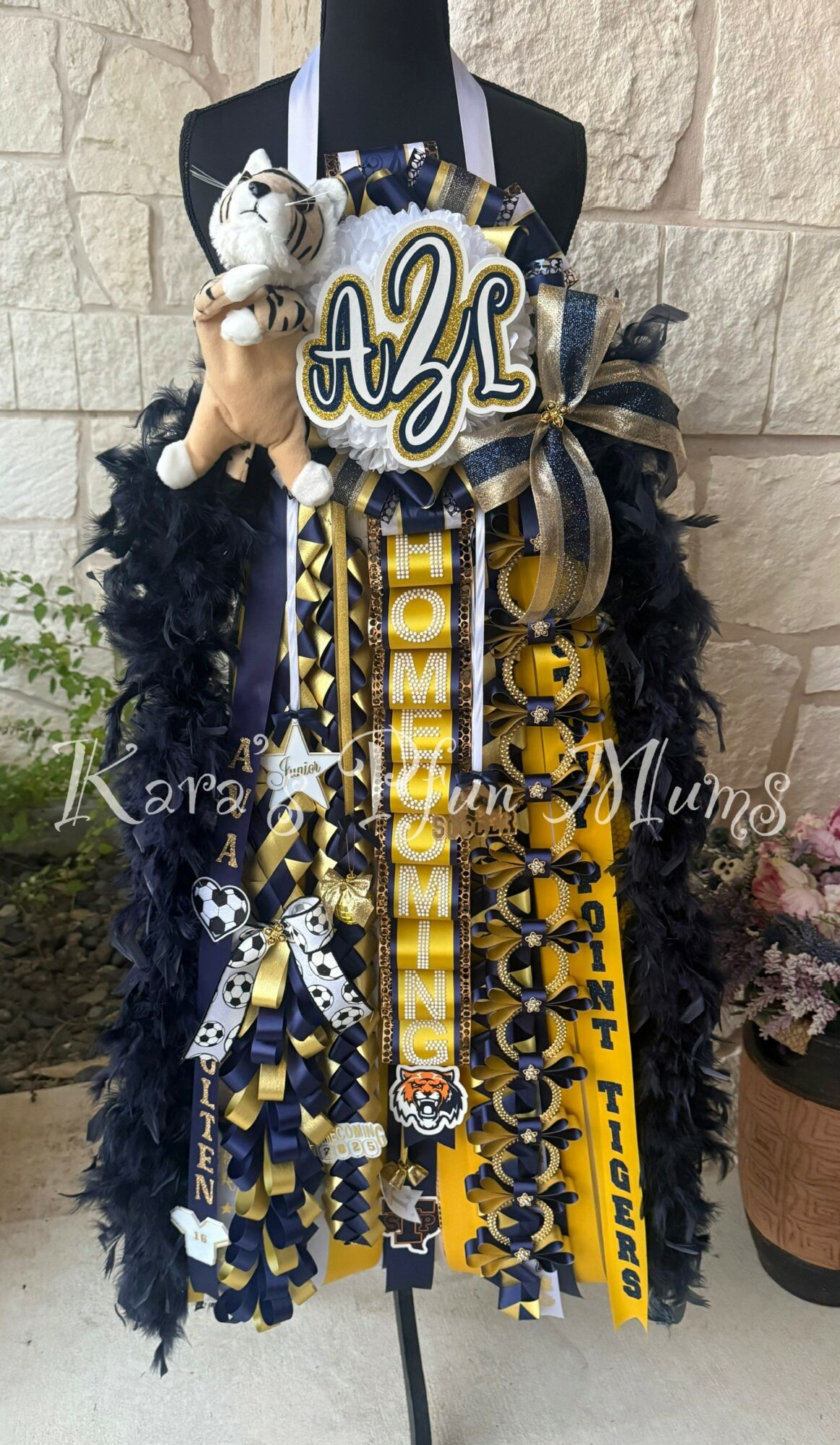 Decorative graduation wreath with ribbons, plush bear, and a large initial letter 'A' on a mannequin.