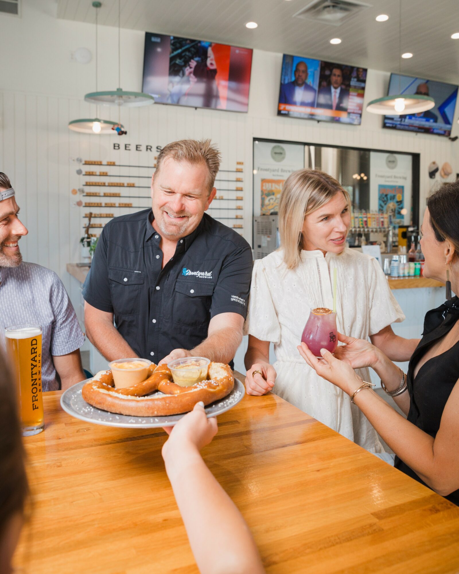Group of people at a bar, with a man and woman holding drinks, engaging in conversation, and smiling.