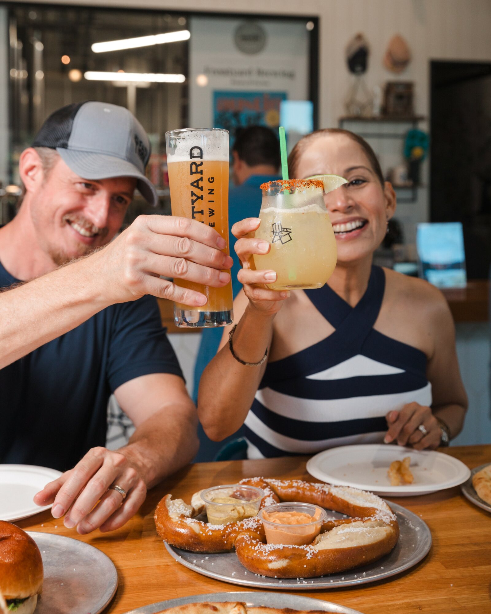 Two people smiling and clinking drinks in a bar, with food on the table.