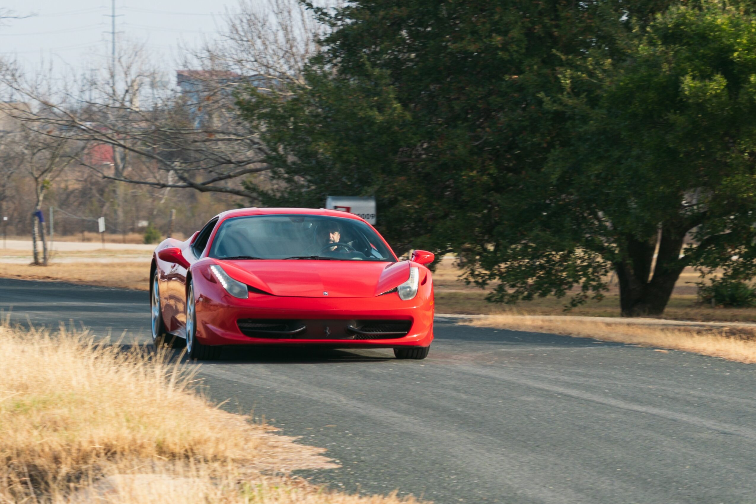 Red sports car driving on a paved road with trees and grass on the side.