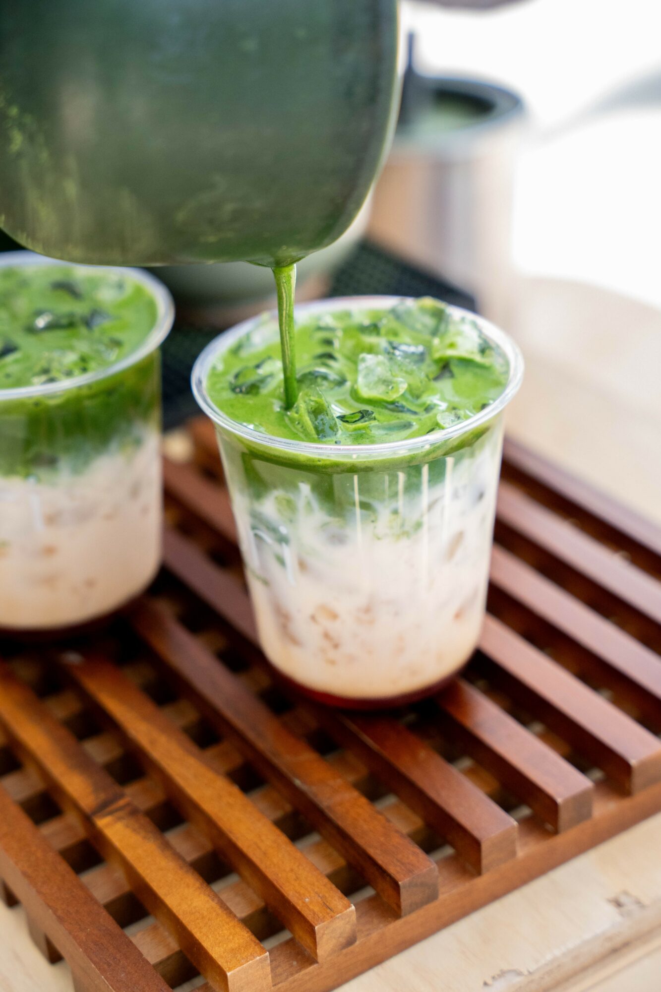 Green beverage with ice being poured into a clear glass on a wooden surface.