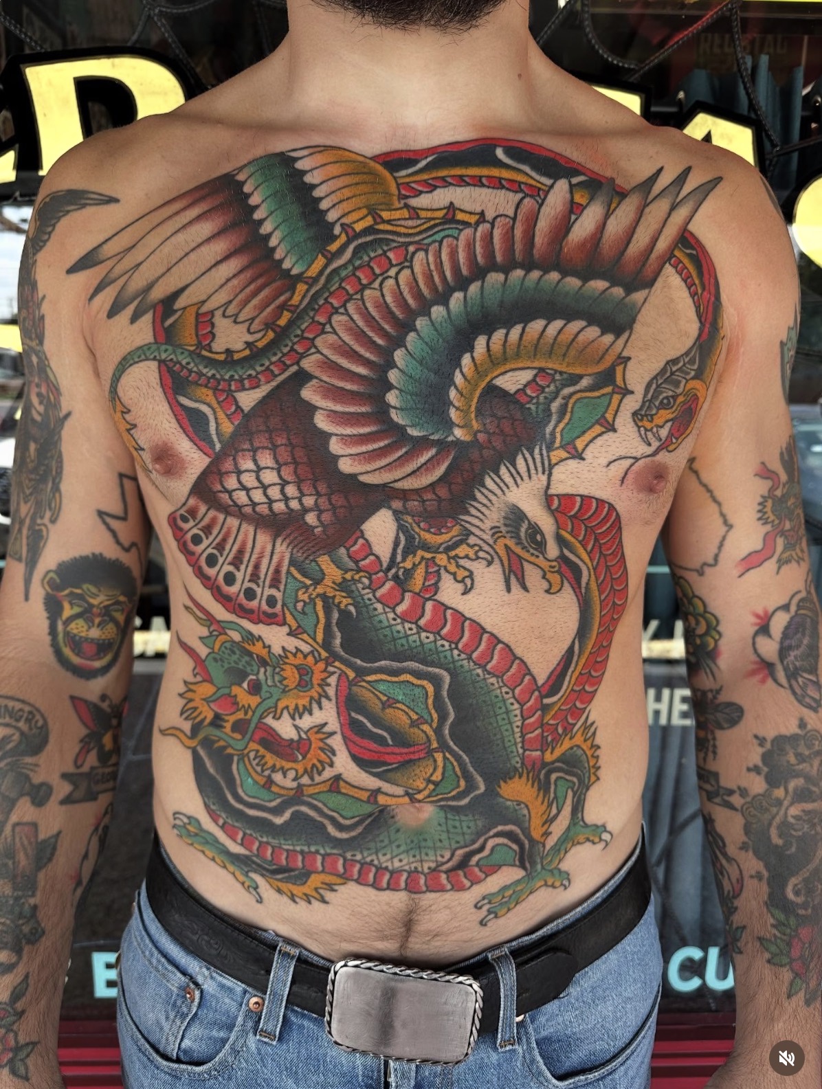 Colorful dragon tattoo covers chest and abdomen with detailed scales, wings, and claws, featuring vibrant reds, greens, and yellows.