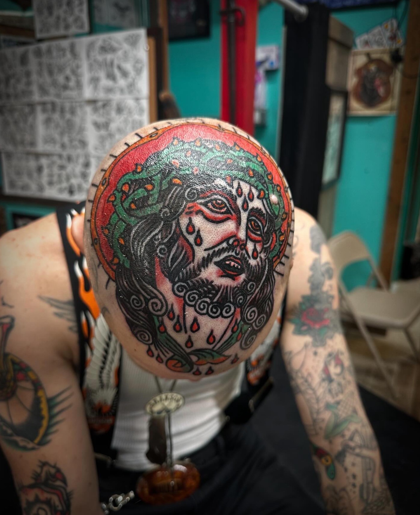 Person with tattooed arms wearing a hat with a detailed face design, surrounded by tattoos and colorful background.