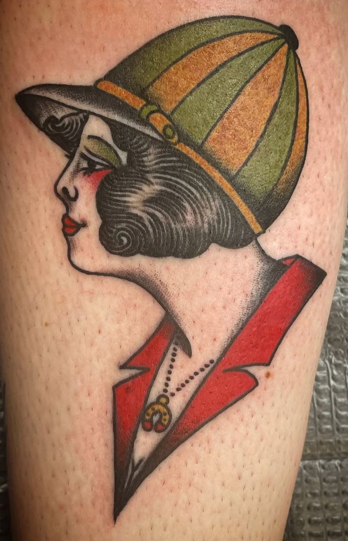 Tattoo of a woman with vintage hairstyle, wearing a striped hat and red jacket, in a classic style.