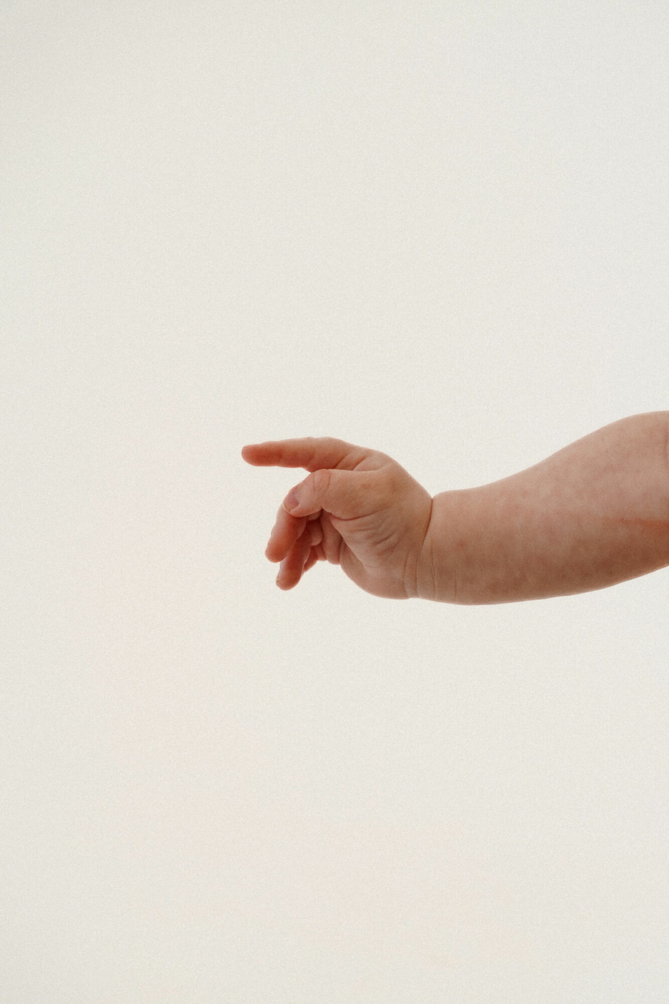 A person's hand with fingers extended, pointing to the left, against a plain white background.