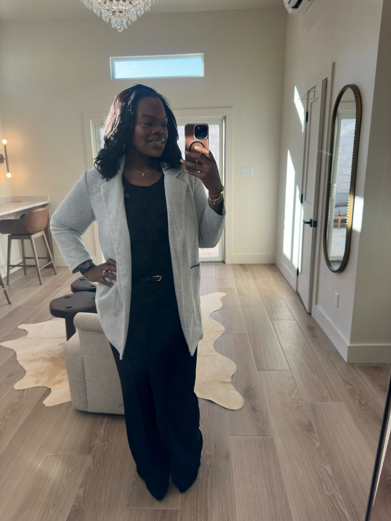 Woman standing in a room with a mirror, wooden floor, and a white rug, holding a phone and smiling.
