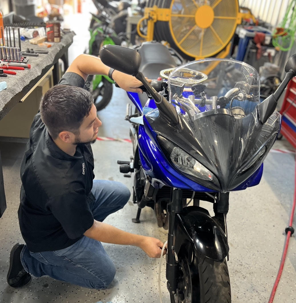 Man working on a blue motorcycle in a workshop with tools and equipment around.