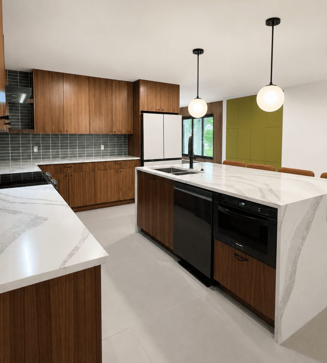 Modern kitchen with wooden cabinets, white countertops, green wall, and two hanging pendant lights.