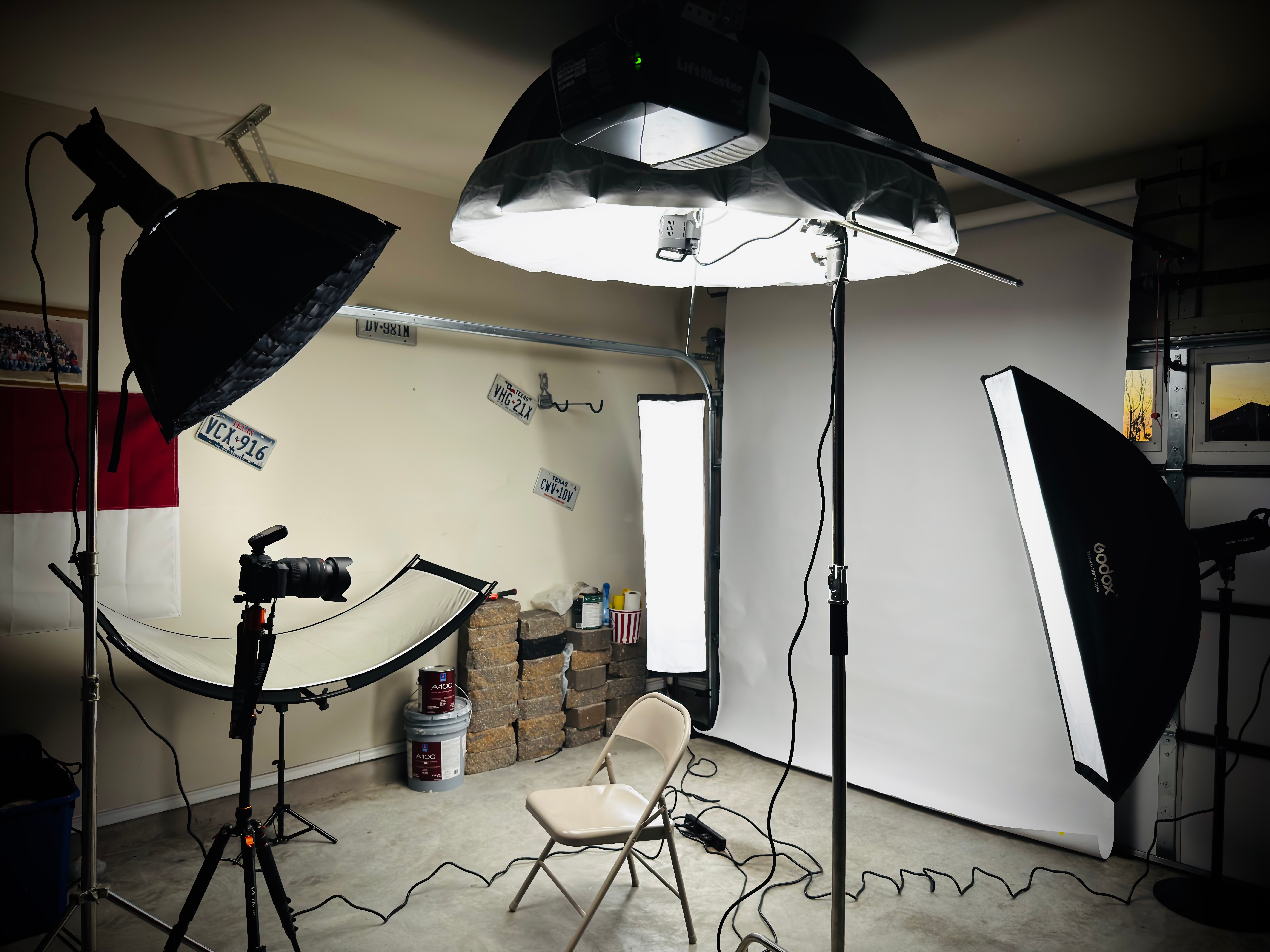 Photography studio with lighting equipment, a chair, and a white backdrop, set up for a photo shoot.