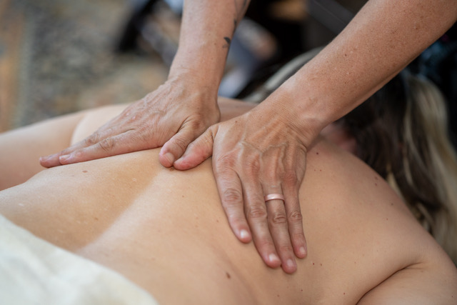 Person receiving a massage on their back, with hands applying pressure, in a close-up view.