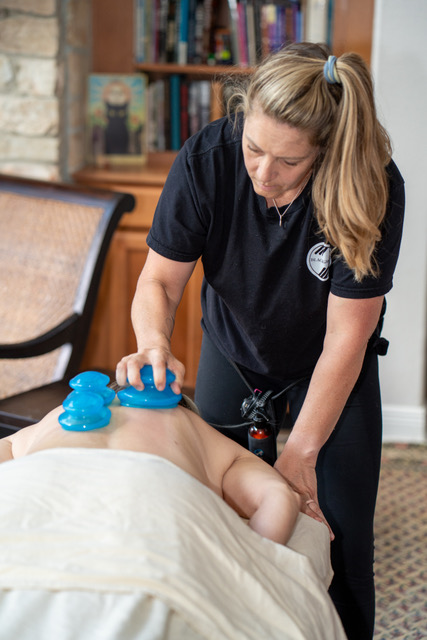 Therapist providing massage therapy to a person lying face down on a massage table in a room with bookshelves.