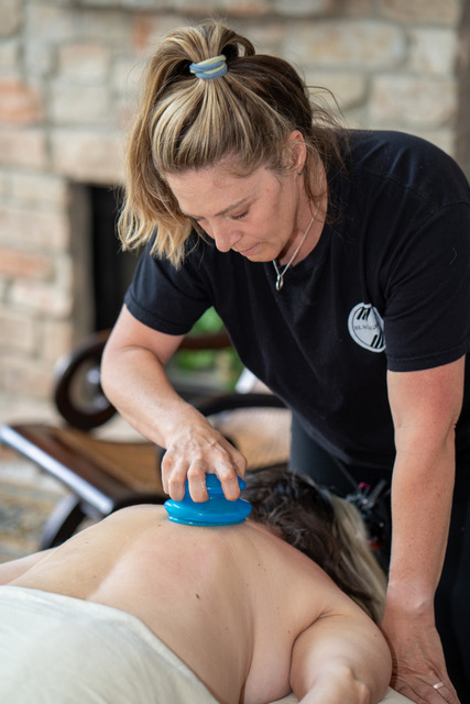 Therapist uses a blue massage tool on a person's back during therapy session.