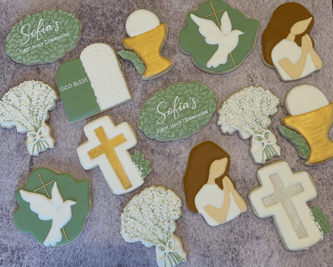 Collection of religious-themed cookies with crosses, doves, and a person praying, on a textured surface.