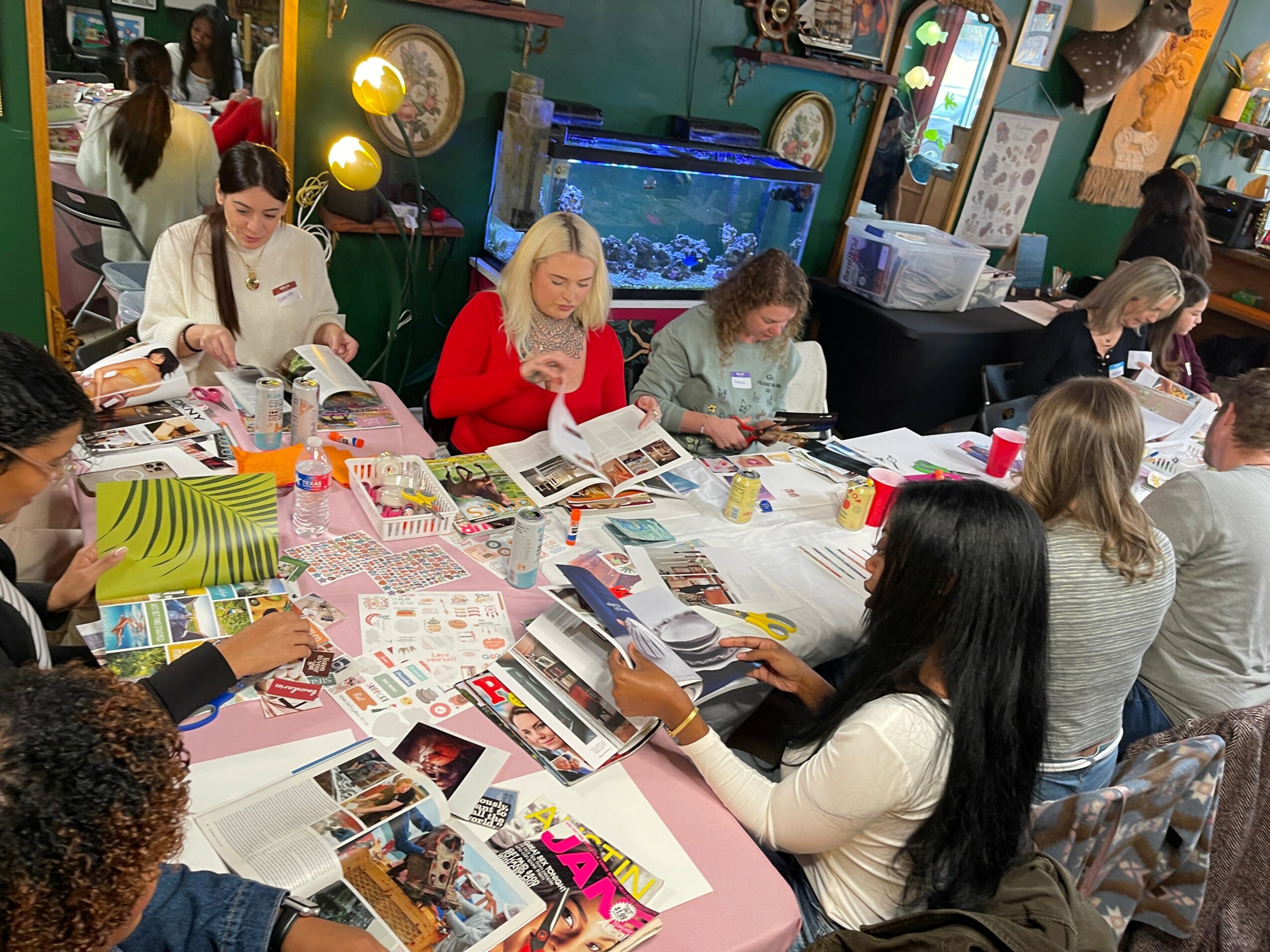 People sitting at a table working on crafts and reading magazines in a colorful room.