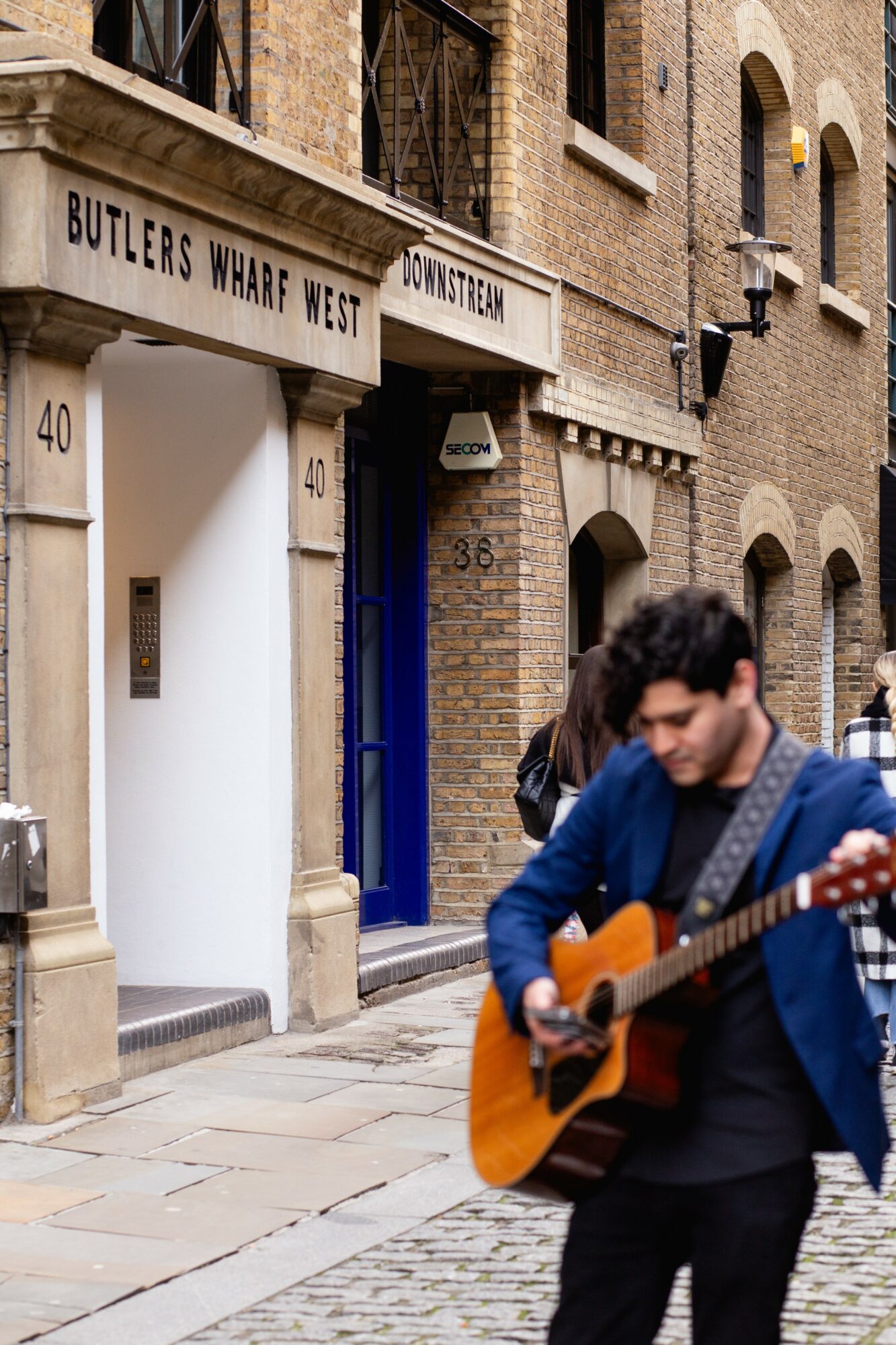 Person playing guitar on street with brick buildings and windows in background.