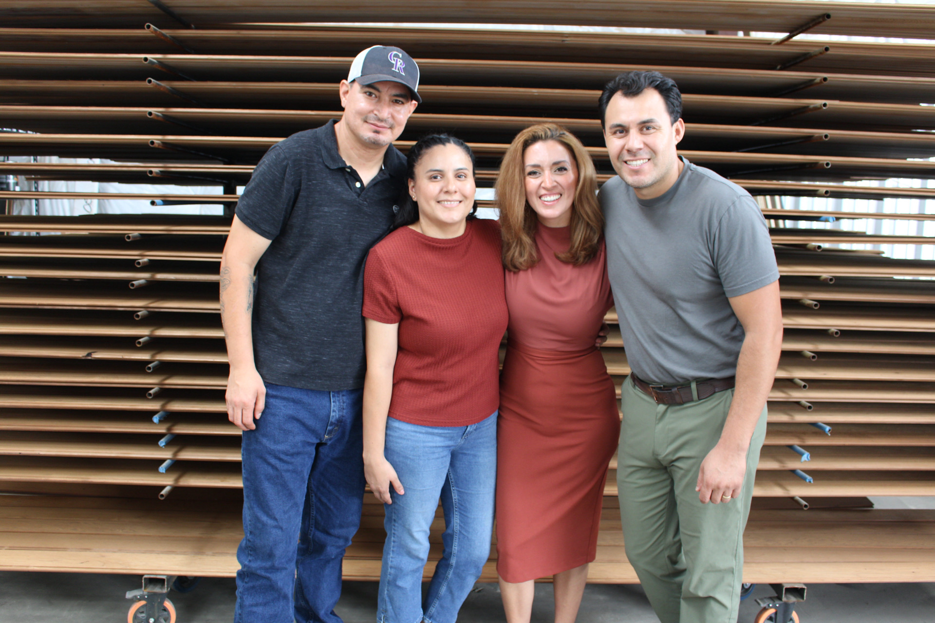 Four people standing together in front of a wooden slatted background, smiling, with two women and two men, casual clothing.