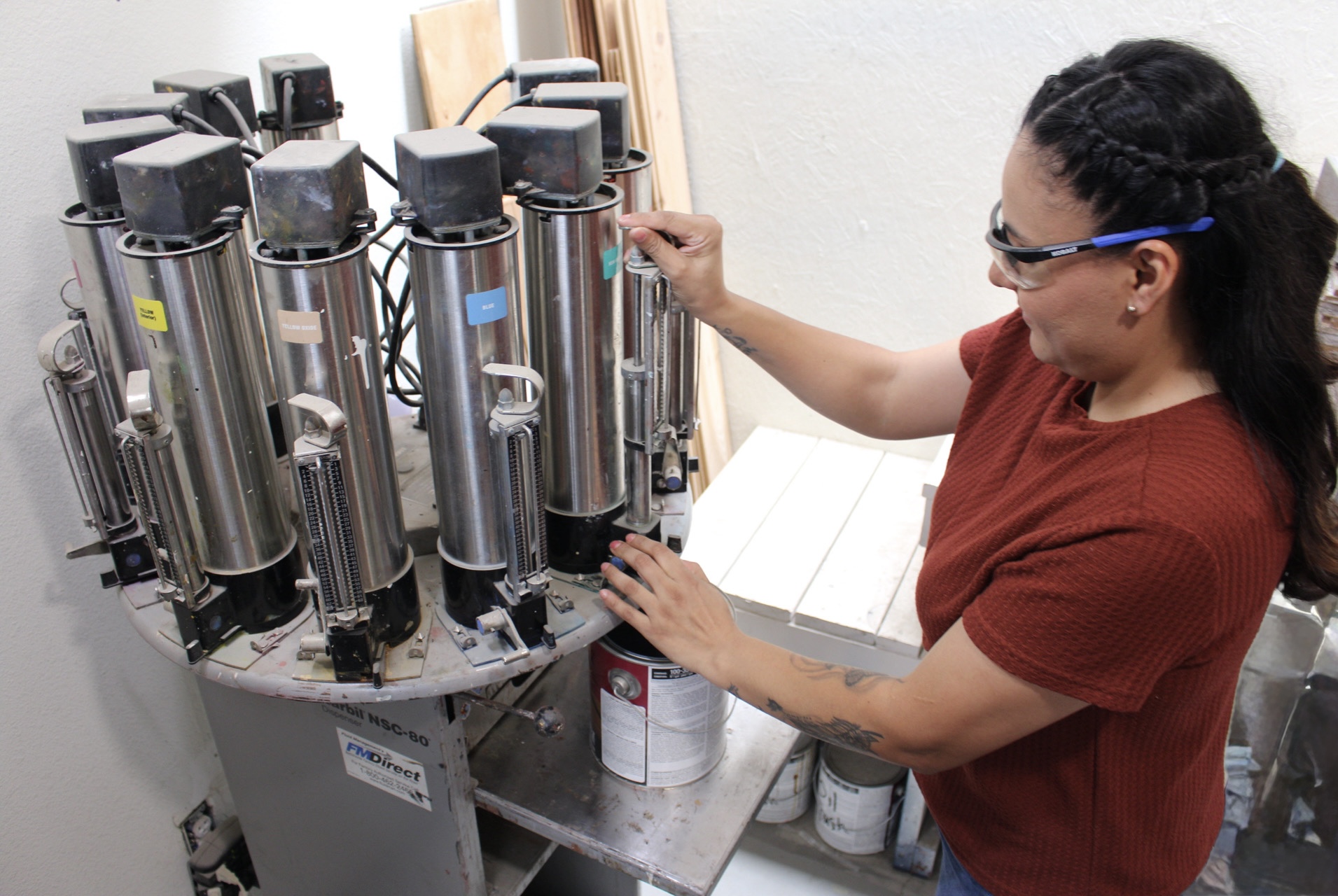 Woman in red shirt and glasses working with multiple stainless steel machines in a lab or workshop.