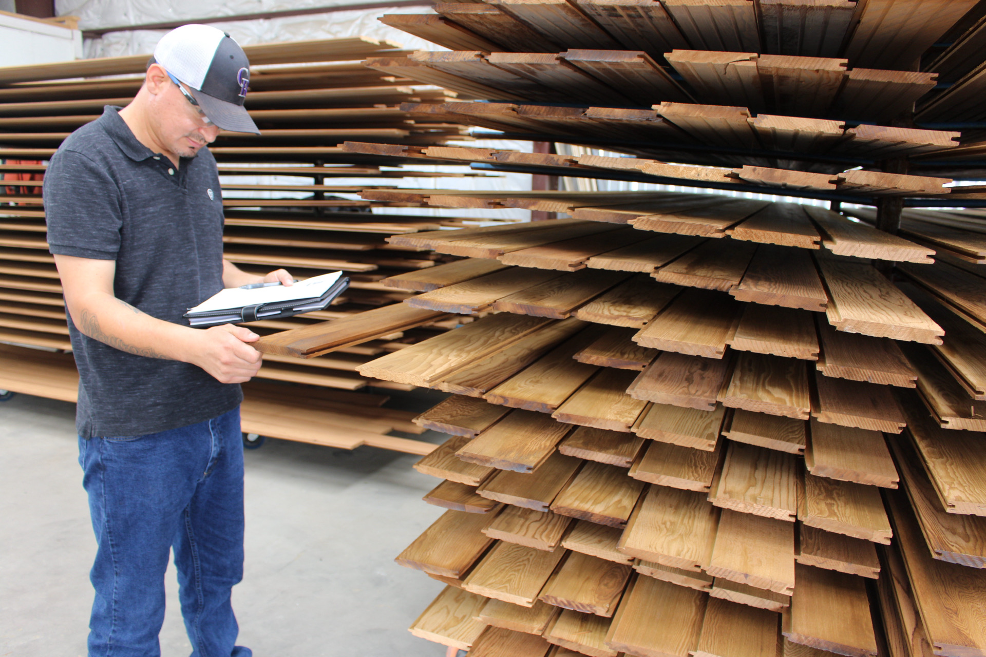 Young man in a cap and casual clothes reads a notebook in front of stacked cardboard sheets.