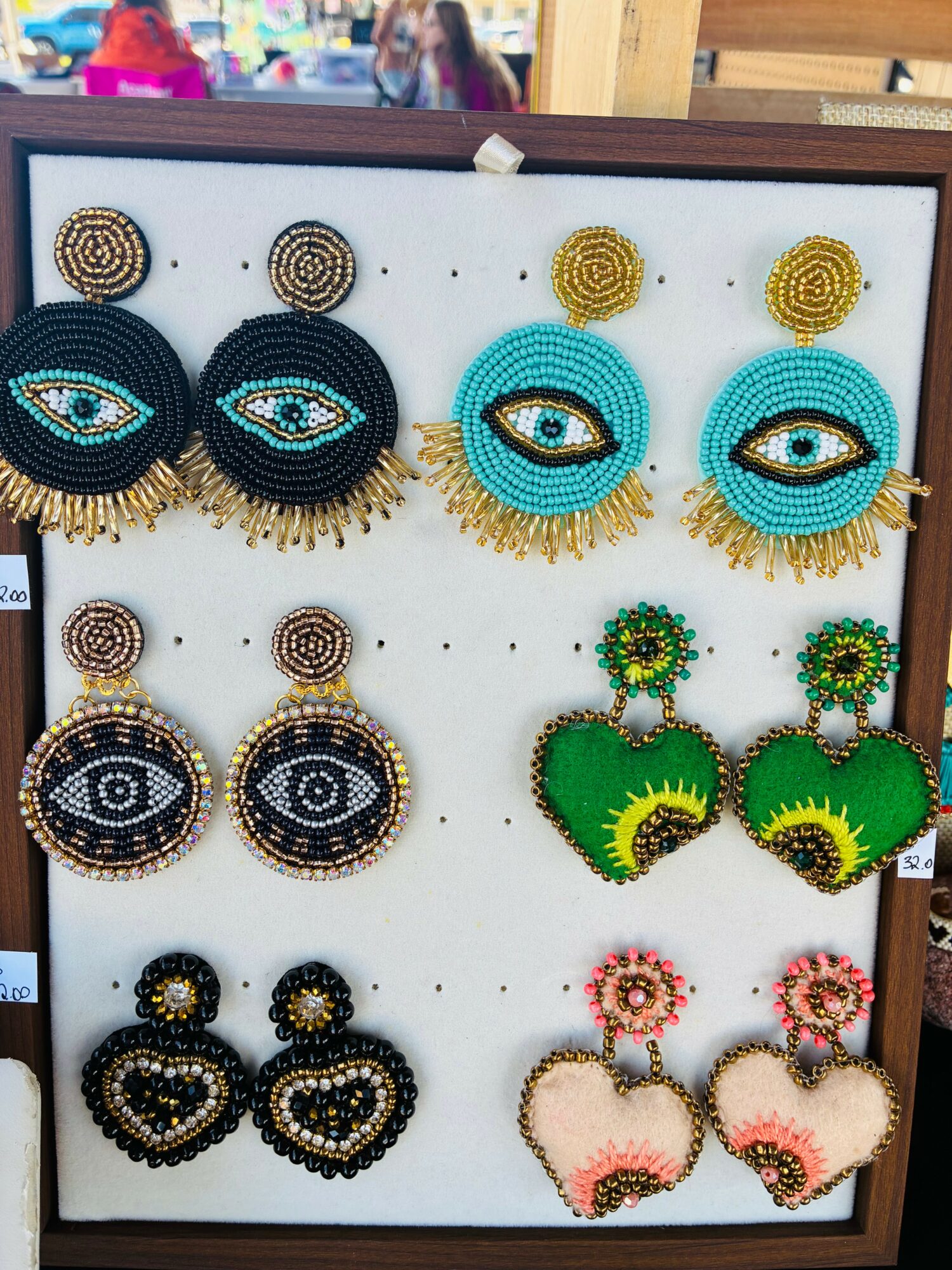 Display of colorful beaded earrings with various eye and heart designs on a white board.