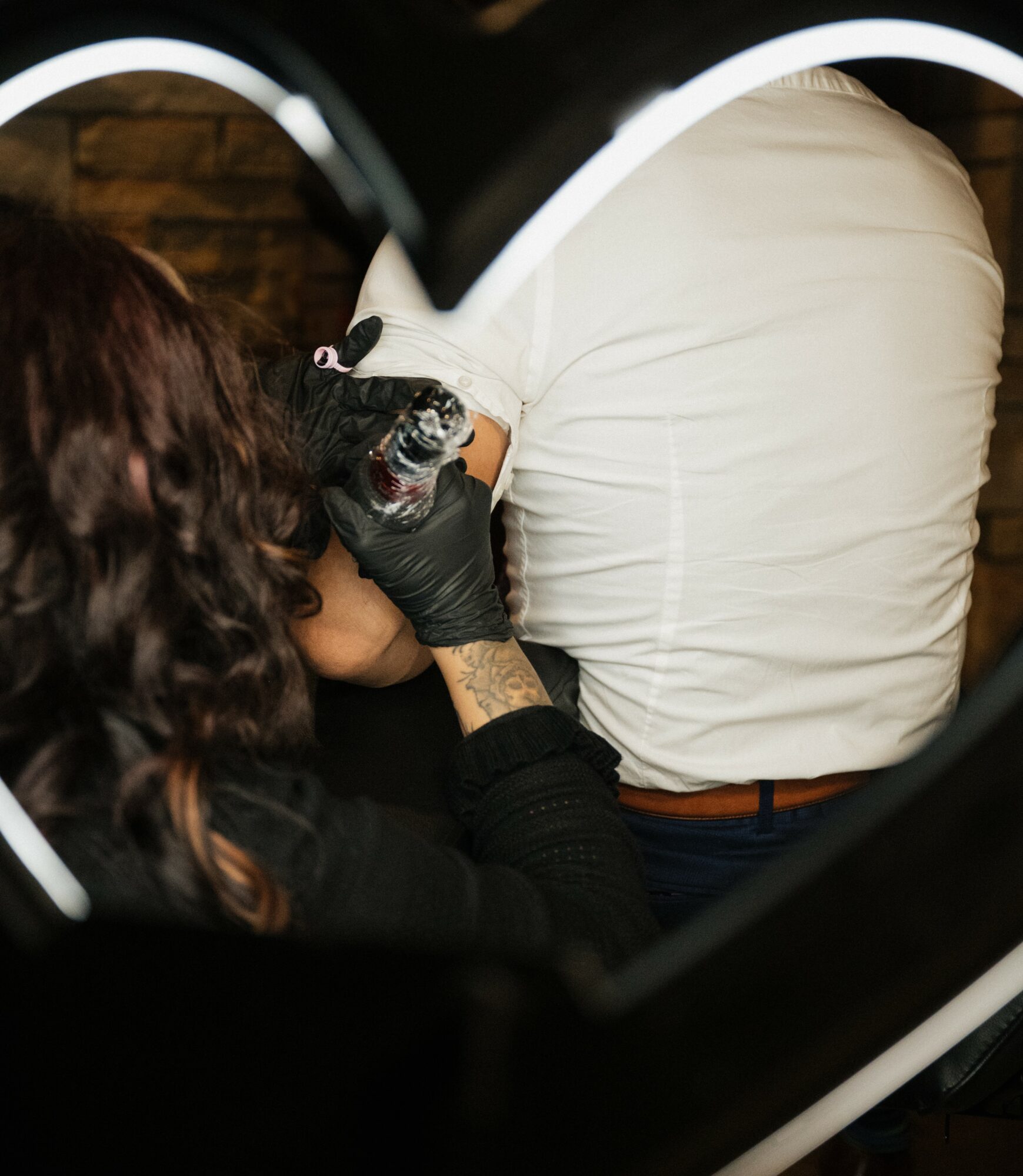 Tattoo artist in black gloves tattoos a person's arm in a tattoo studio with brick wall background.