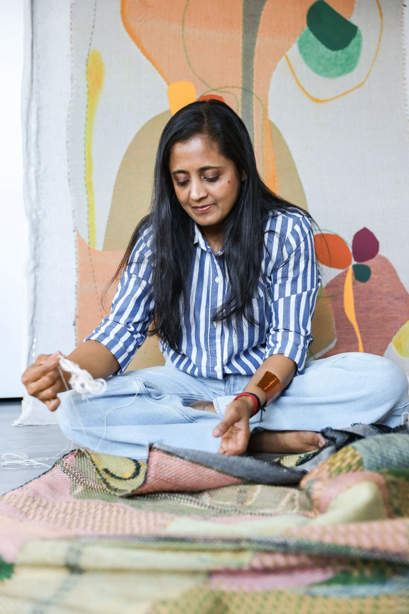 Woman sitting cross-legged on the floor, looking down, with colorful abstract wall art behind her.