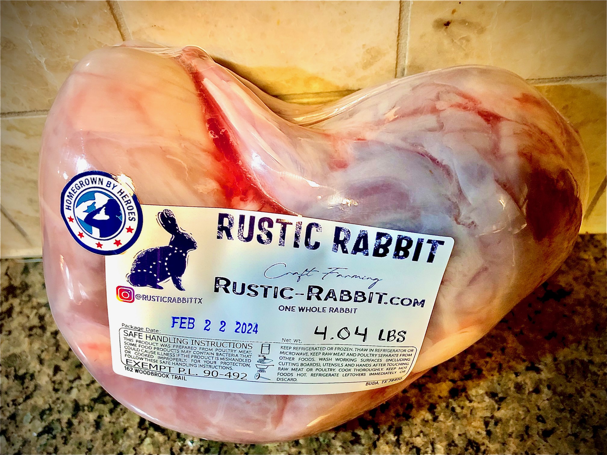 Raw rabbit meat with a label, placed on a kitchen countertop, showing weight and date, with tiled wall background.