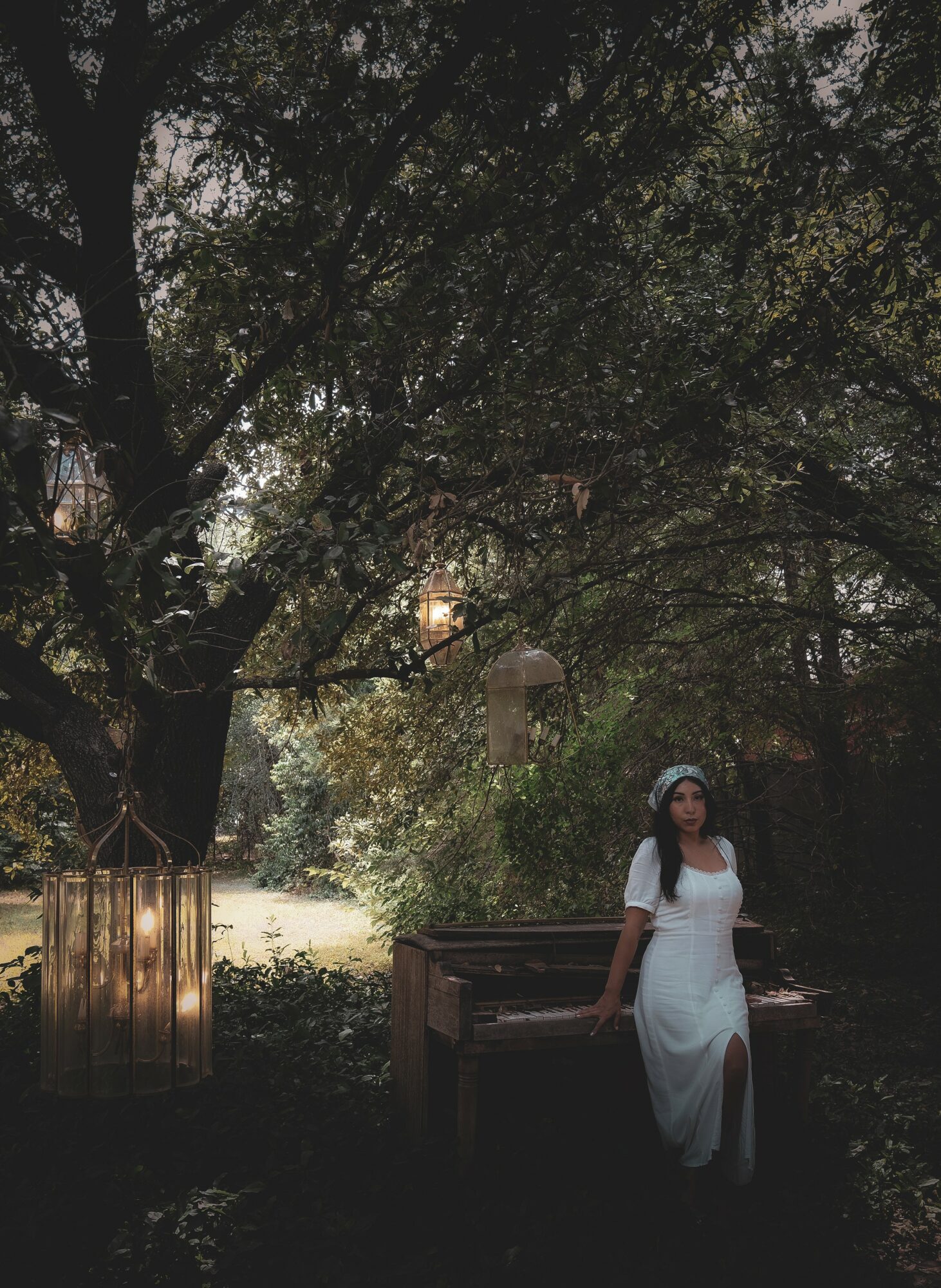 Woman in white dress standing outdoors near a wooden bench and trees, with sunlight filtering through leaves.