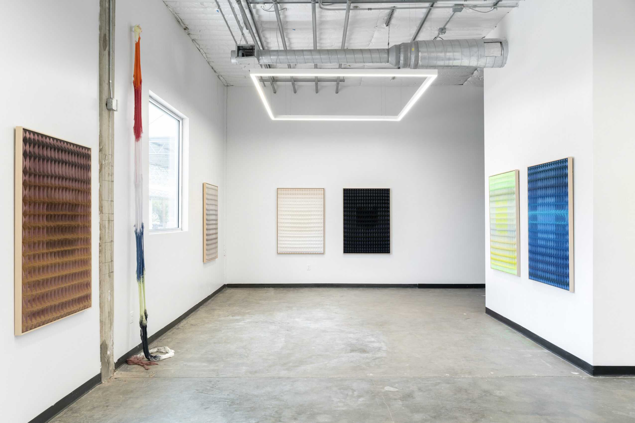 Gallery room with white walls, artwork on walls, concrete floor, and ceiling light fixture, viewed from corner.