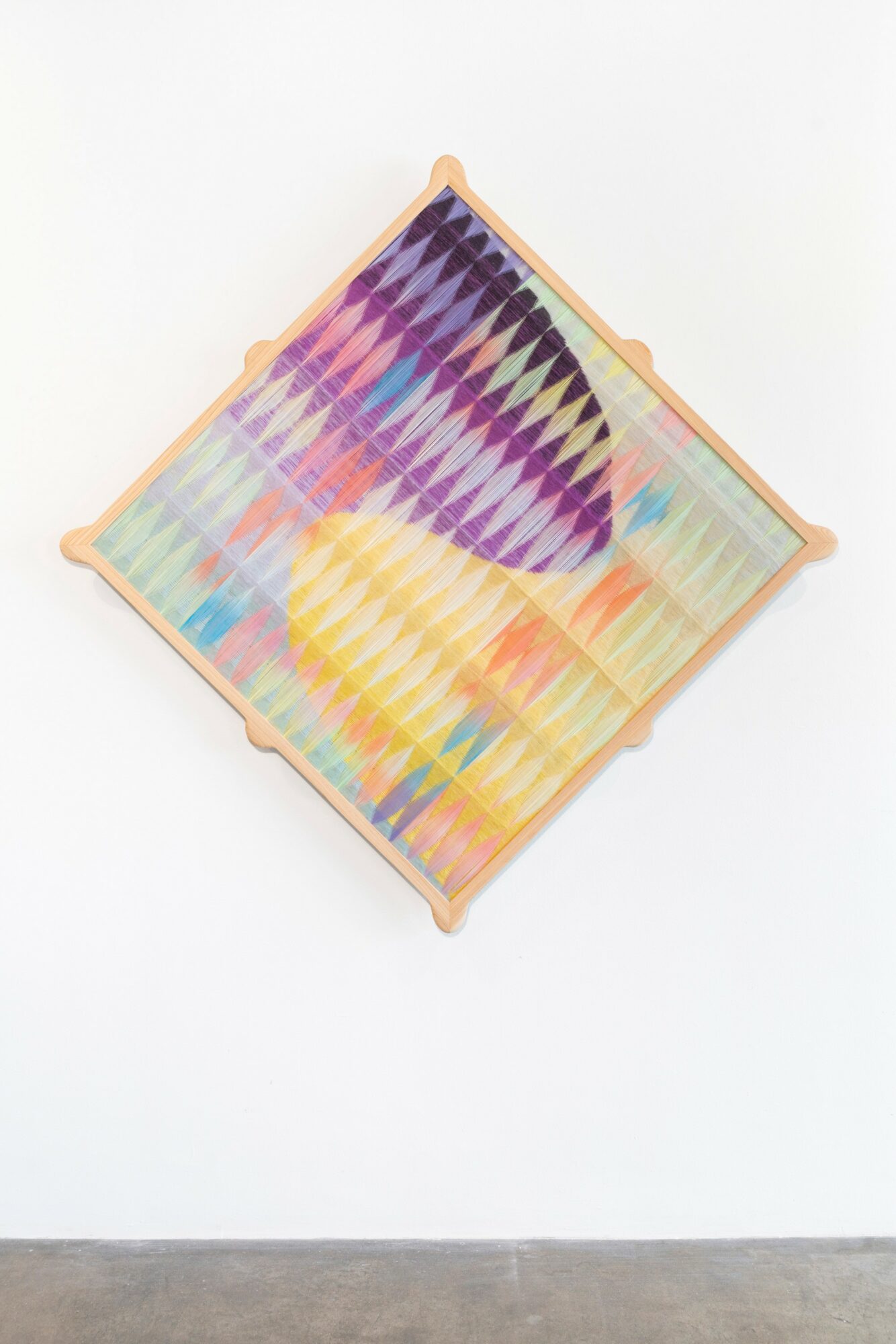 Colorful abstract artwork with geometric patterns on a square canvas, tilted on a white wall.