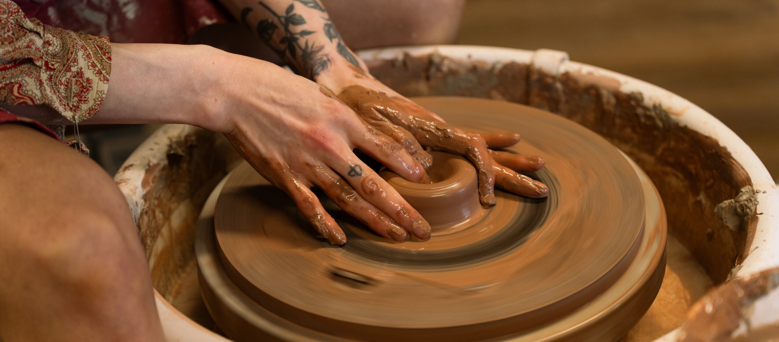 Person shaping clay on a pottery wheel with hands covered in clay, working on a ceramic piece.