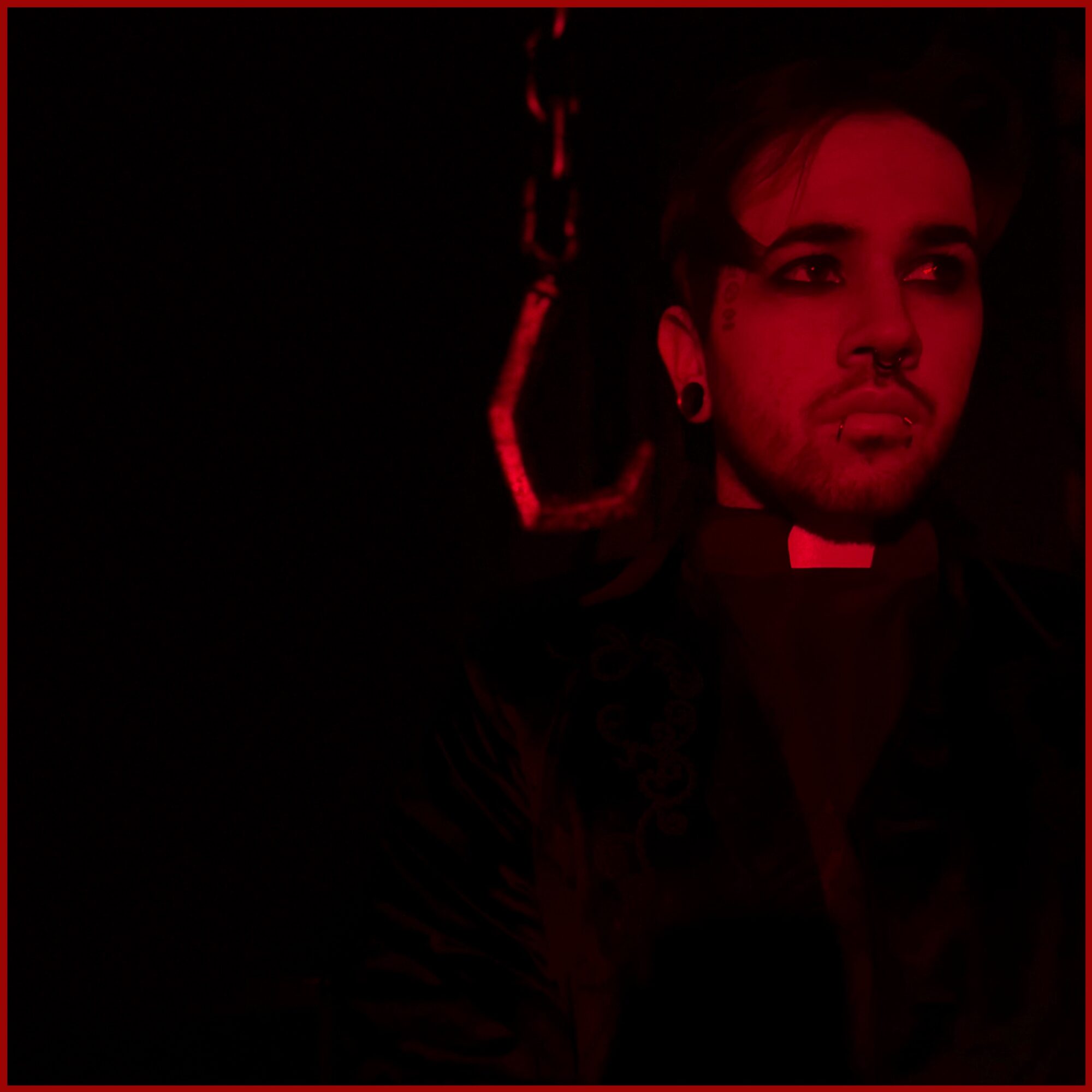 Person with dark hair and earrings, illuminated by red light, looking to the side, dark background.