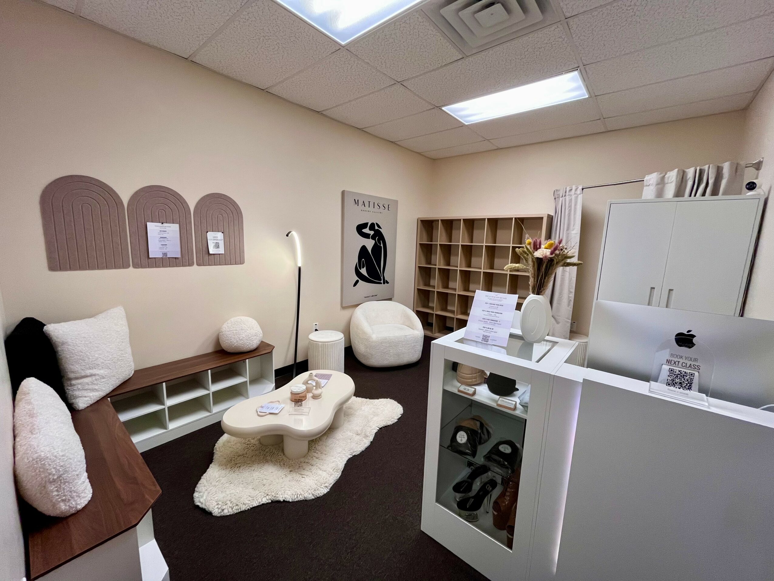 Office room with seating, shelves, a desk, and a computer, decorated with artwork and soft furnishings.
