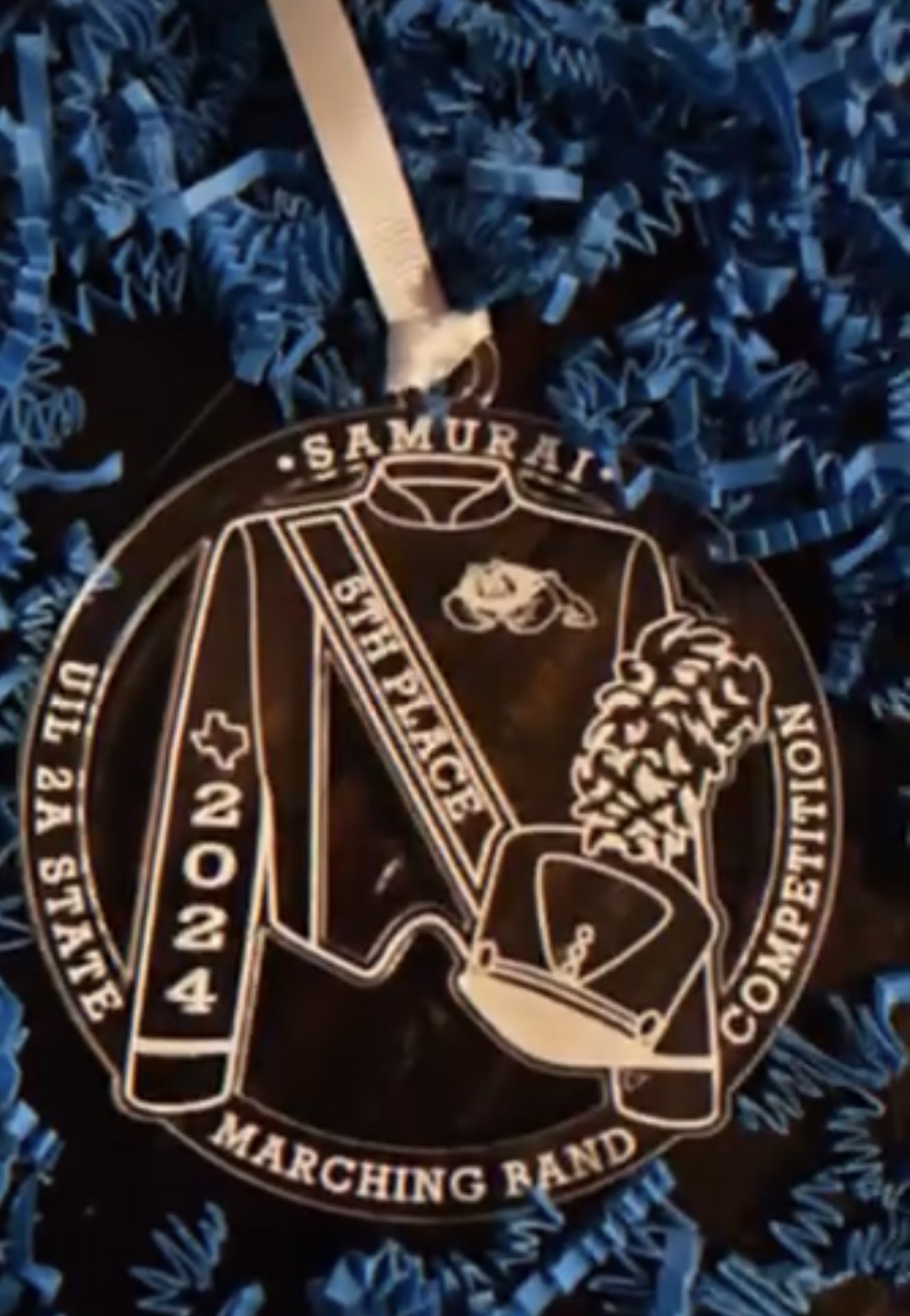Medal with text and design, hanging on a ribbon, surrounded by blue patterned fabric.