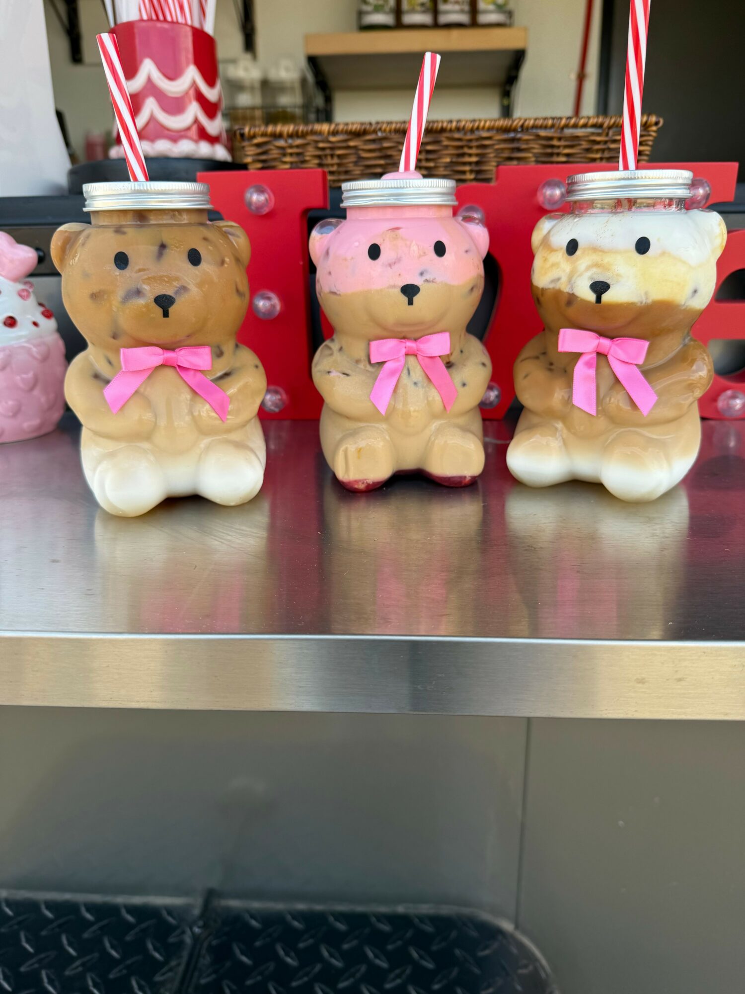 Three teddy bear cakes with pink bows and striped straws on a metallic surface.