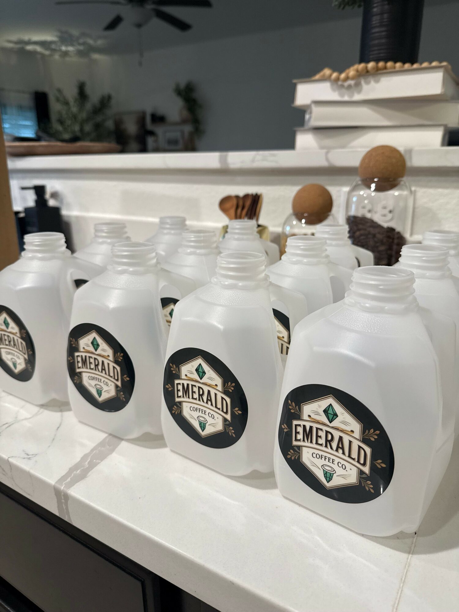 Multiple bottles of Emerald brand liquid soap or sanitizer on a white counter, with a blurred background of a kitchen or workspace.